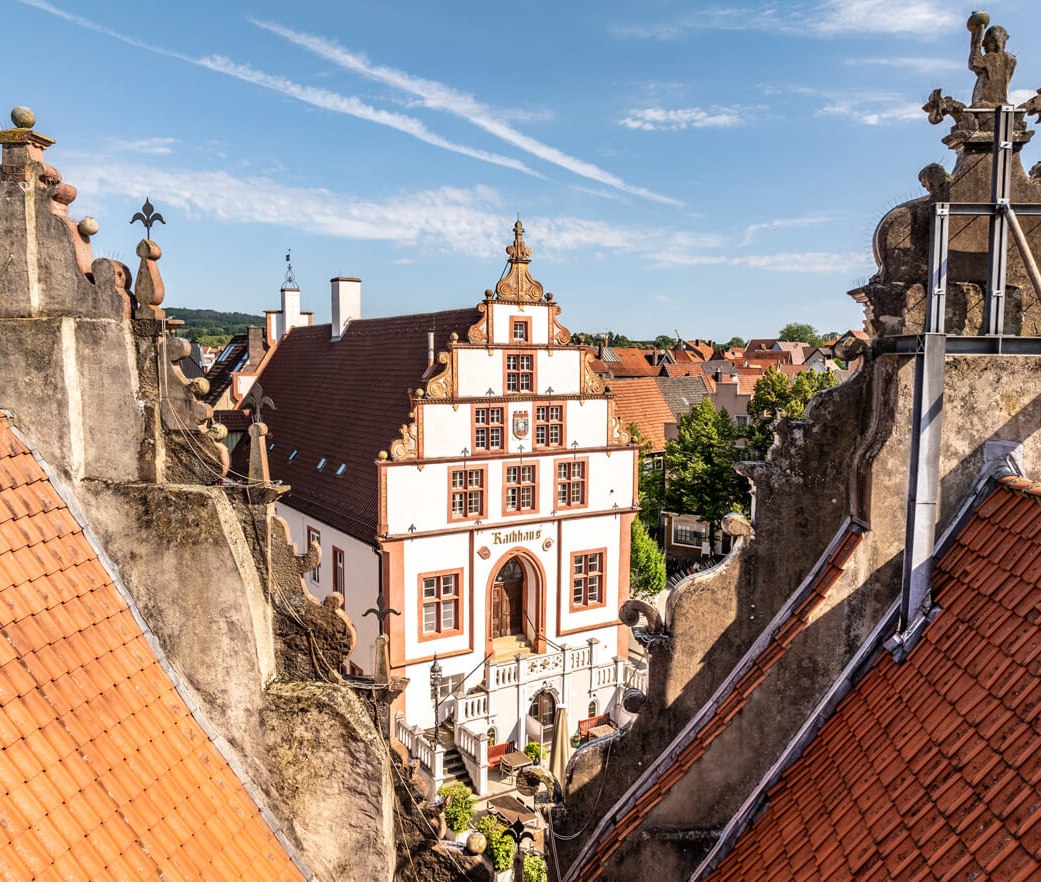 Das historische Rathaus als Drohnenaufnahme zwischen zwei gegenüberliegenden Schmuckgiebeln hindurch fotografiert