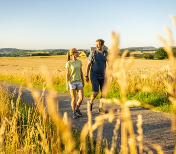 2 Personen wandern im Abendlicht im Hochsommer durch die Felder am Waldrand von Wüsten