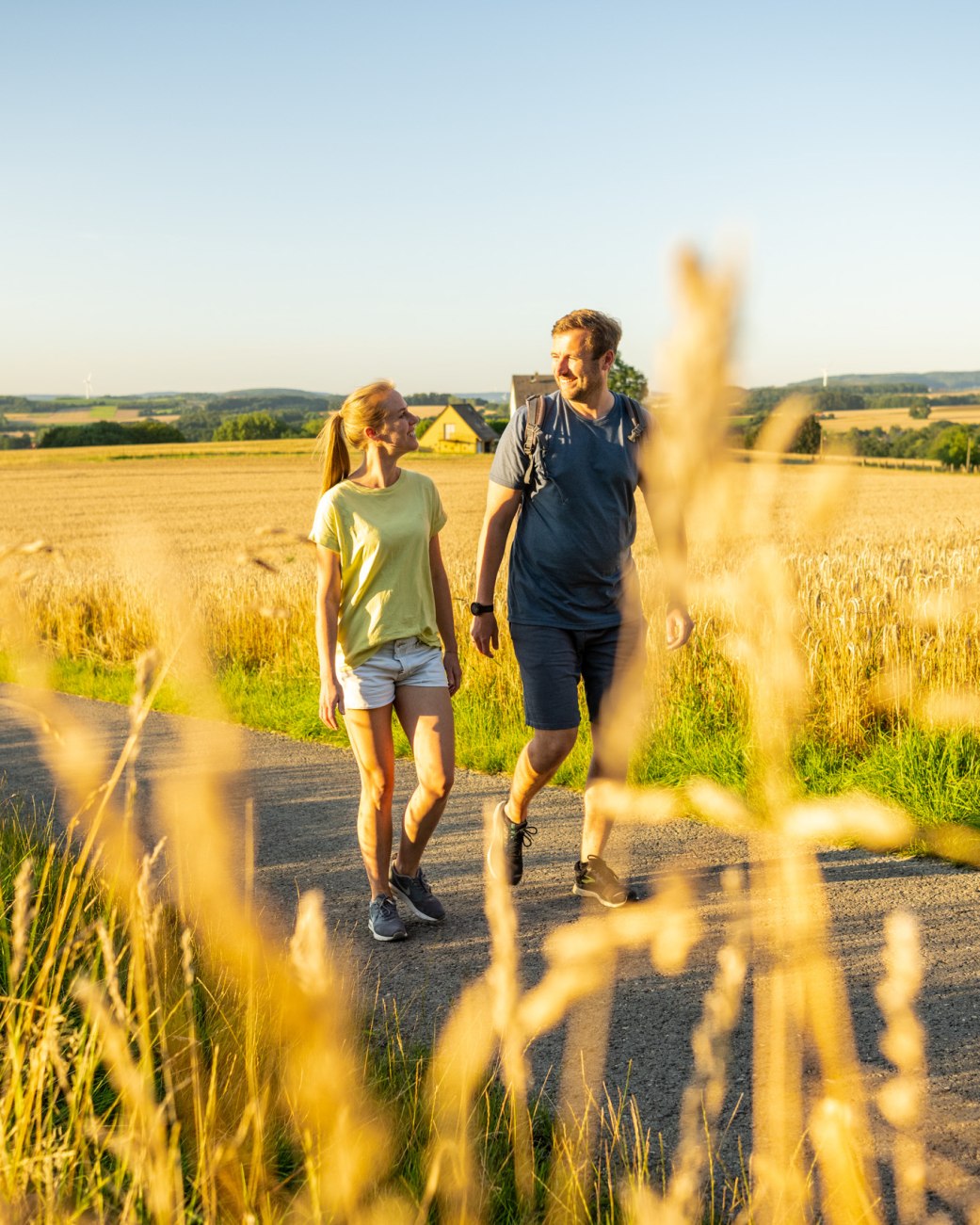 2 Personen wandern im Abendlicht im Hochsommer durch die Felder am Waldrand von Wüsten