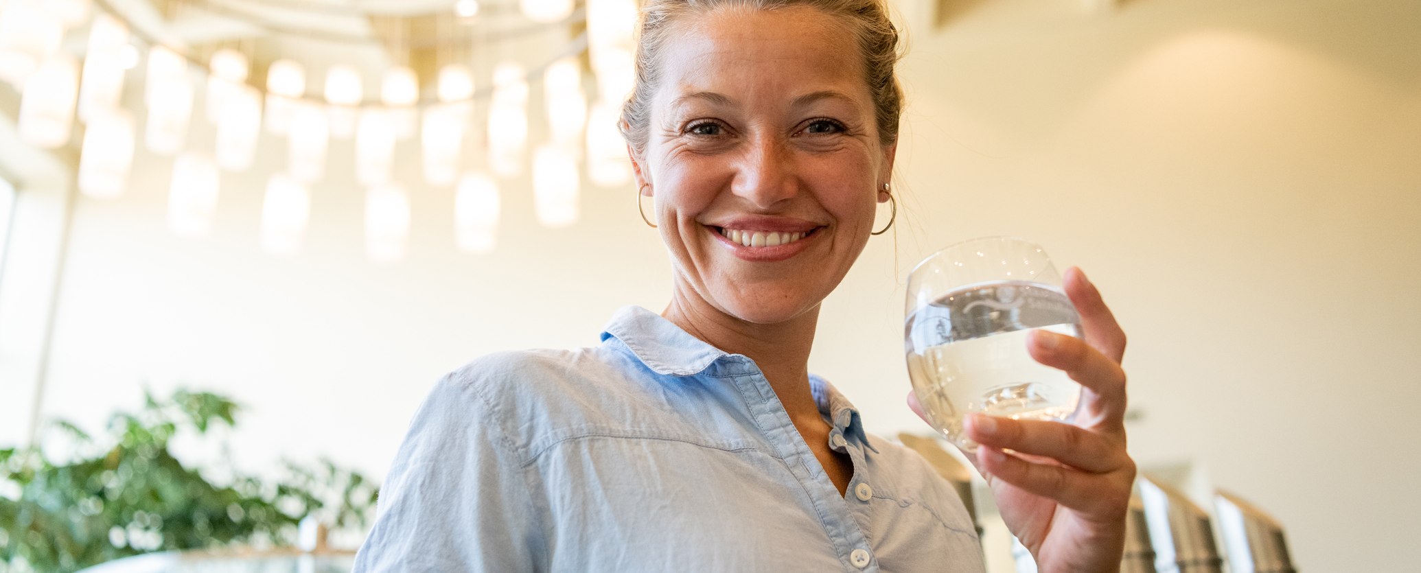 Frau hält ein Glas Sole in der Wandelhalle und lächelt in die Kamera